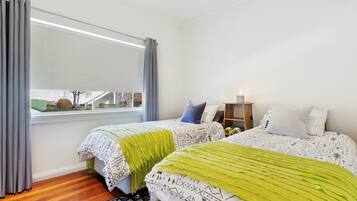 A bedroom with two beds, a window with curtains, a bedside table with a lamp, and a view of the outside.