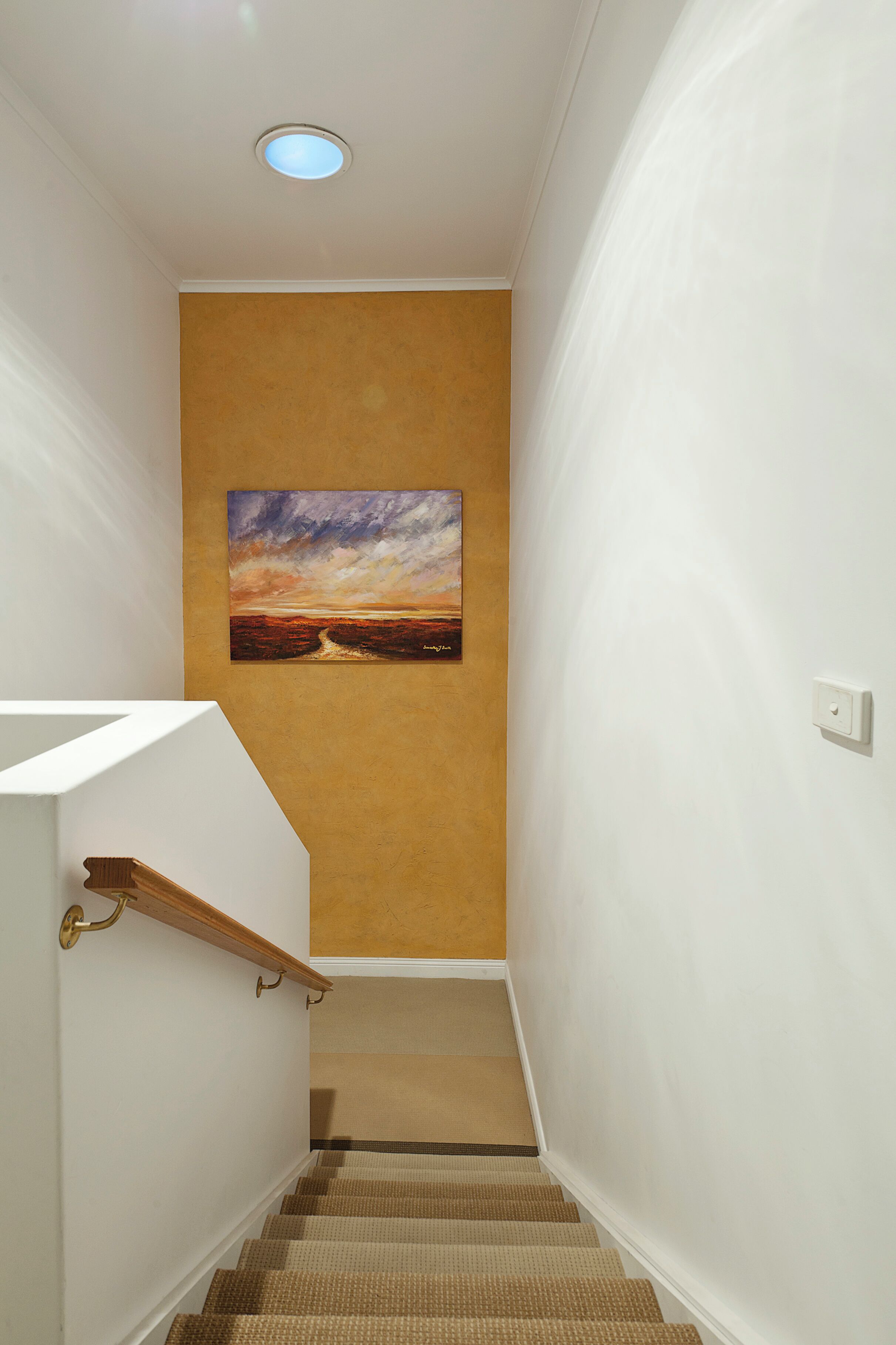 A staircase with a beige carpet and a painting of a sunset on the wall.