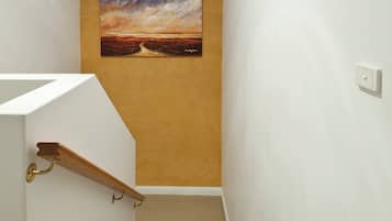 Een trap met een beigekleurig tapijt en een schilderij van een zonsondergang aan de muur.