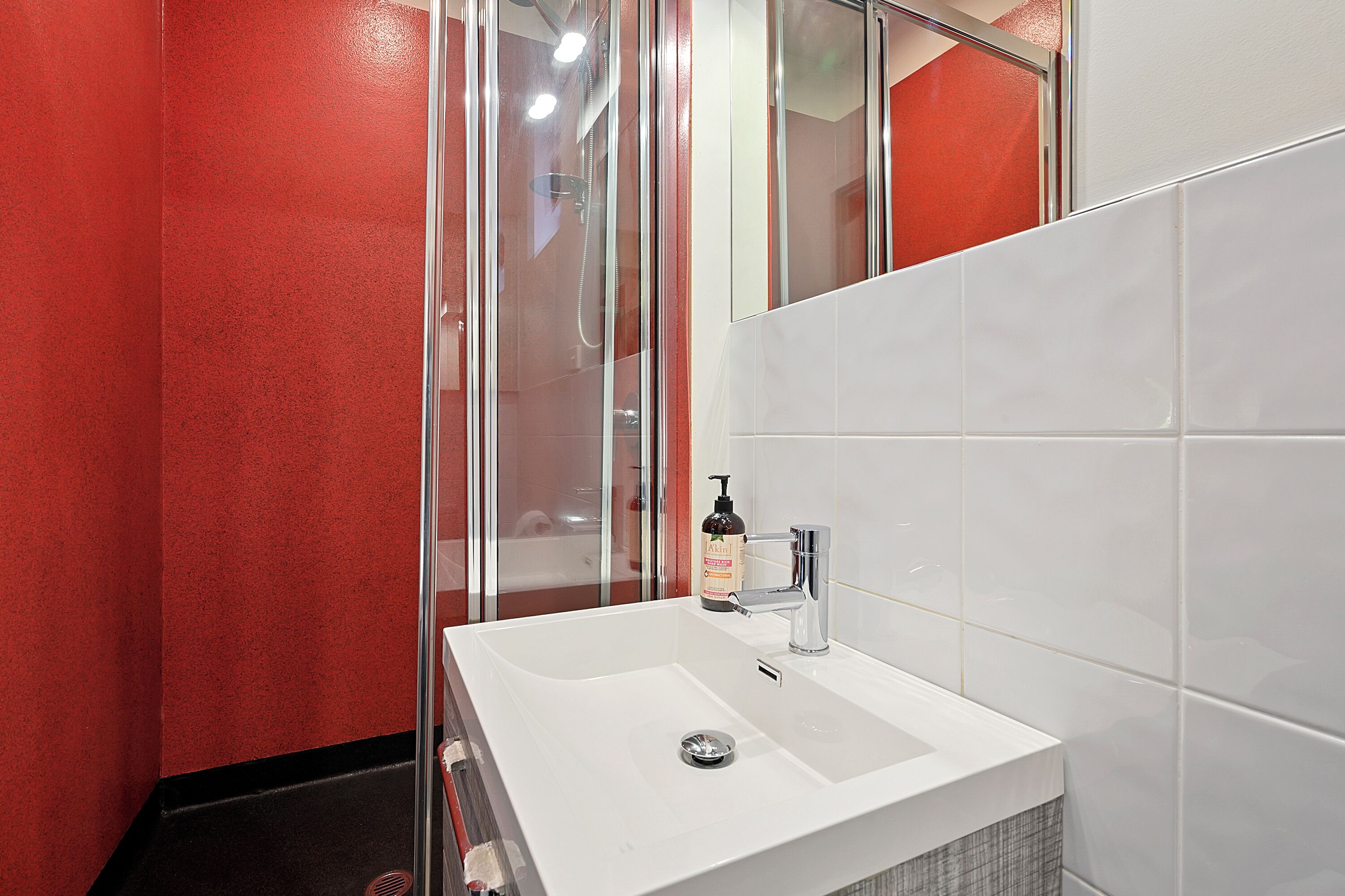 A bathroom with a white sink, a glass shower enclosure, and red walls.