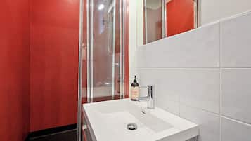 A bathroom with a white sink, a glass shower enclosure, and red walls.