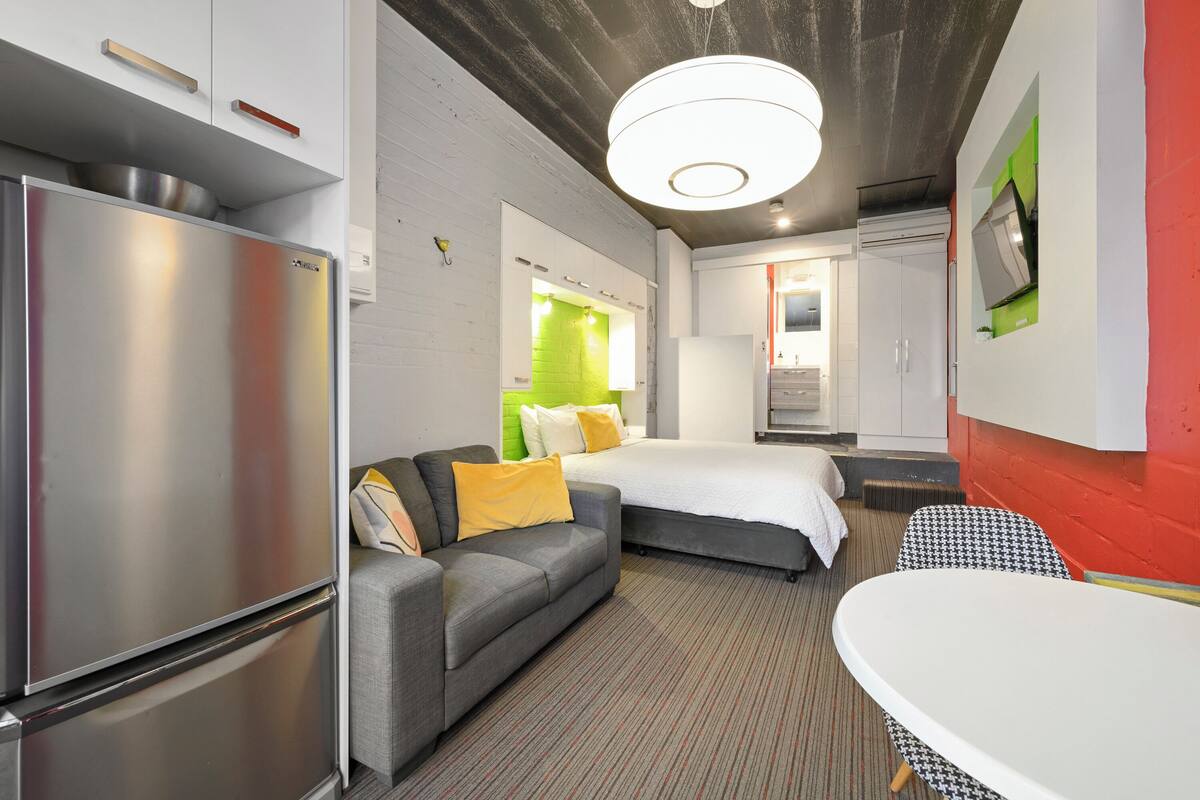 Een moderne hotelkamer met een groot bed, een slaapbank, een eettafel en een ingebouwde koelkast.