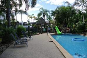 A pool area with lounge chairs, a slide, and a thatched-roof structure.