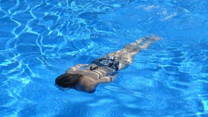 A person swimming in a clear blue pool.