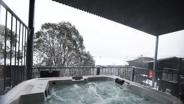 Ett bubbelbad med utsikt över ett snötäckt landskap och en byggnad i bakgrunden.