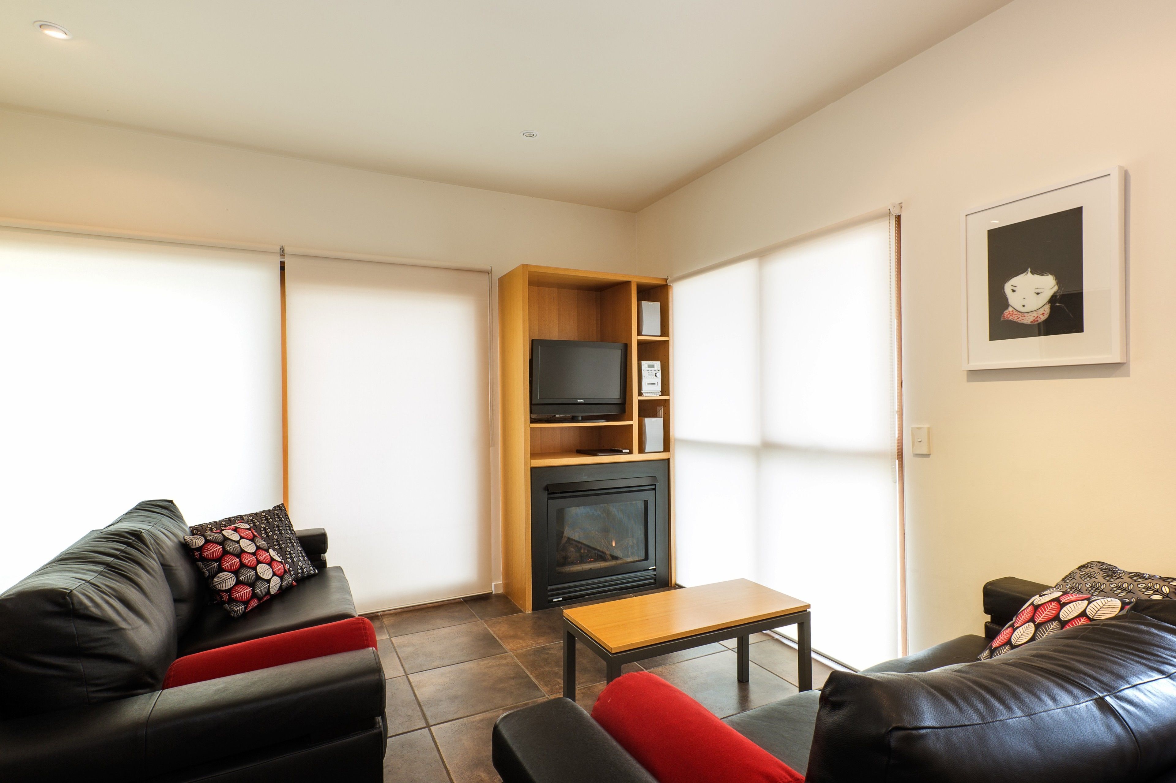 Een moderne woonkamer met een open haard, zwarte leren banken en een houten entertainmentmeubel.