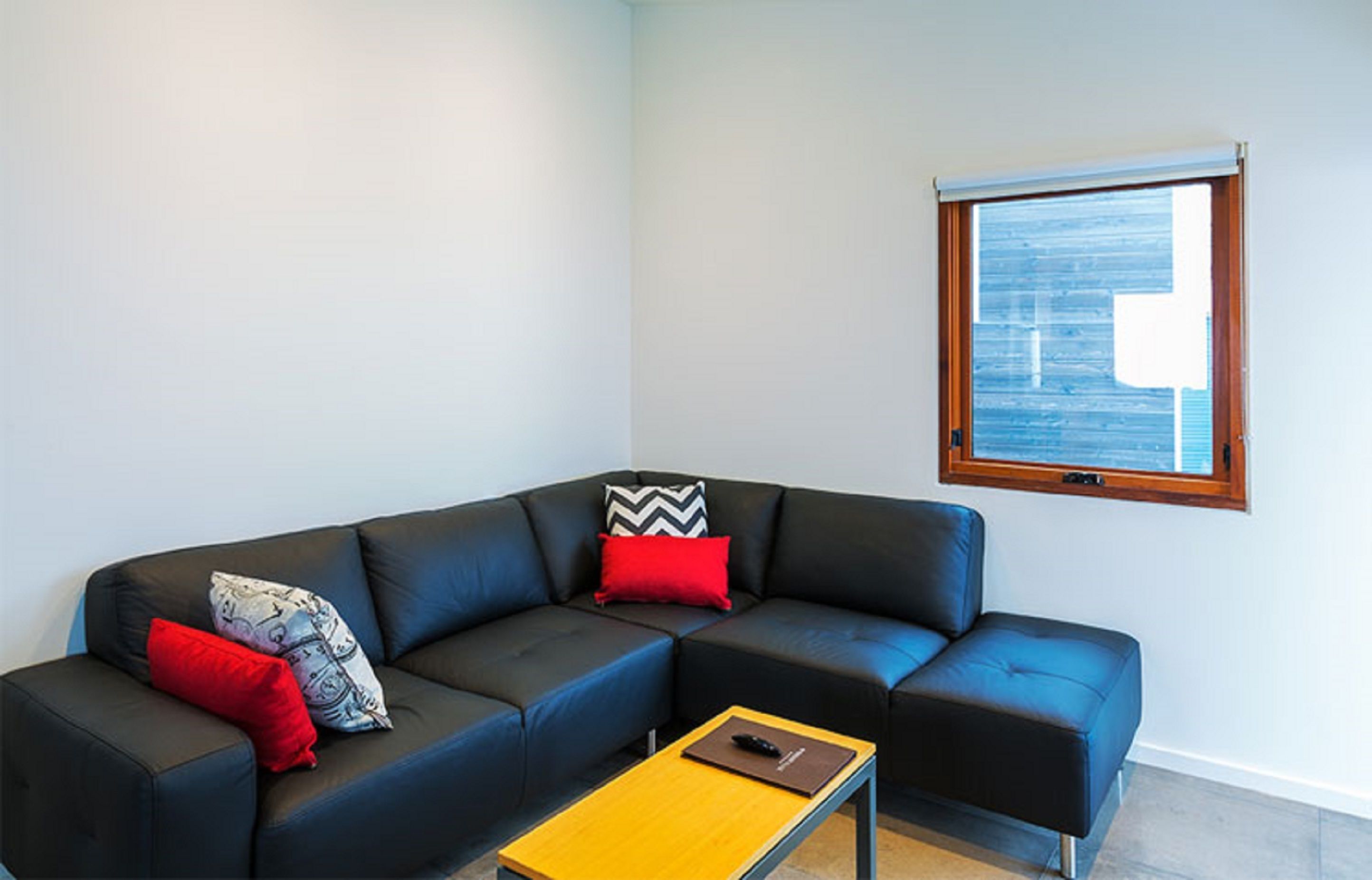 A modern living room with a sectional sofa, a small table, and a window with blinds.