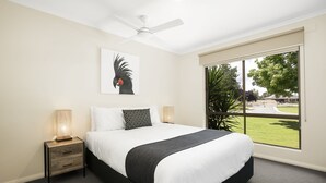 A bedroom with a bed, nightstands, a ceiling fan, and a large window with a view of greenery. - Lakeside Country Club - Numurkah (Numurkah)