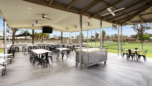 An outdoor covered dining area with tables and chairs, ceiling fans, and a view of a sports field. - Lakeside Country Club - Numurkah (Numurkah)