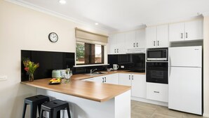 A modern kitchen with white cabinets, a wooden countertop, a built-in oven, a microwave, and a refrigerator. - Lakeside Country Club - Numurkah (Numurkah)
