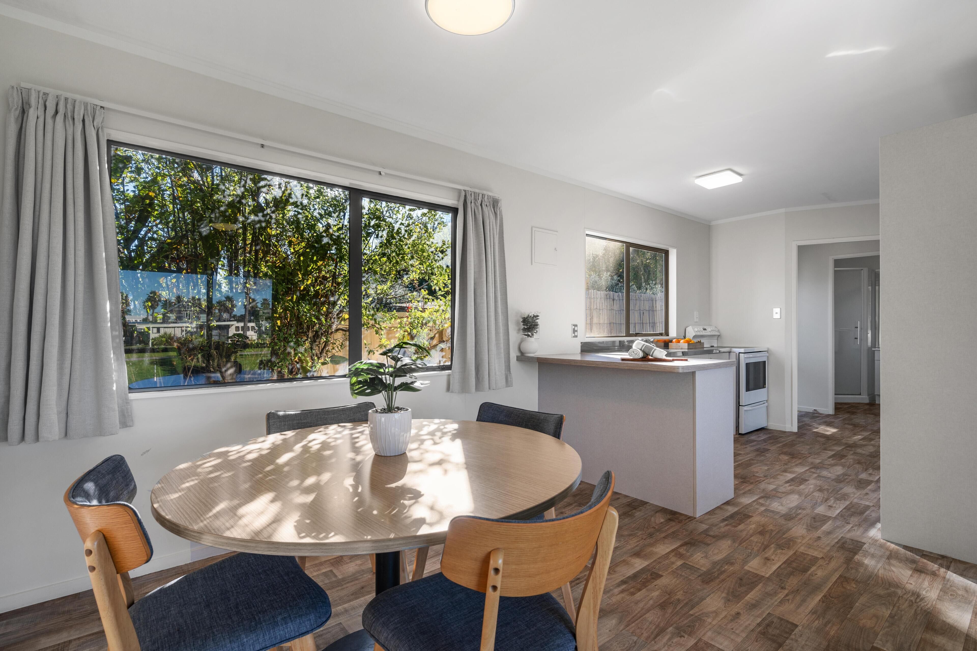 Una cocina moderna con una isla central, un comedor con mesa redonda y sillas, y ventanas grandes con cortinas.