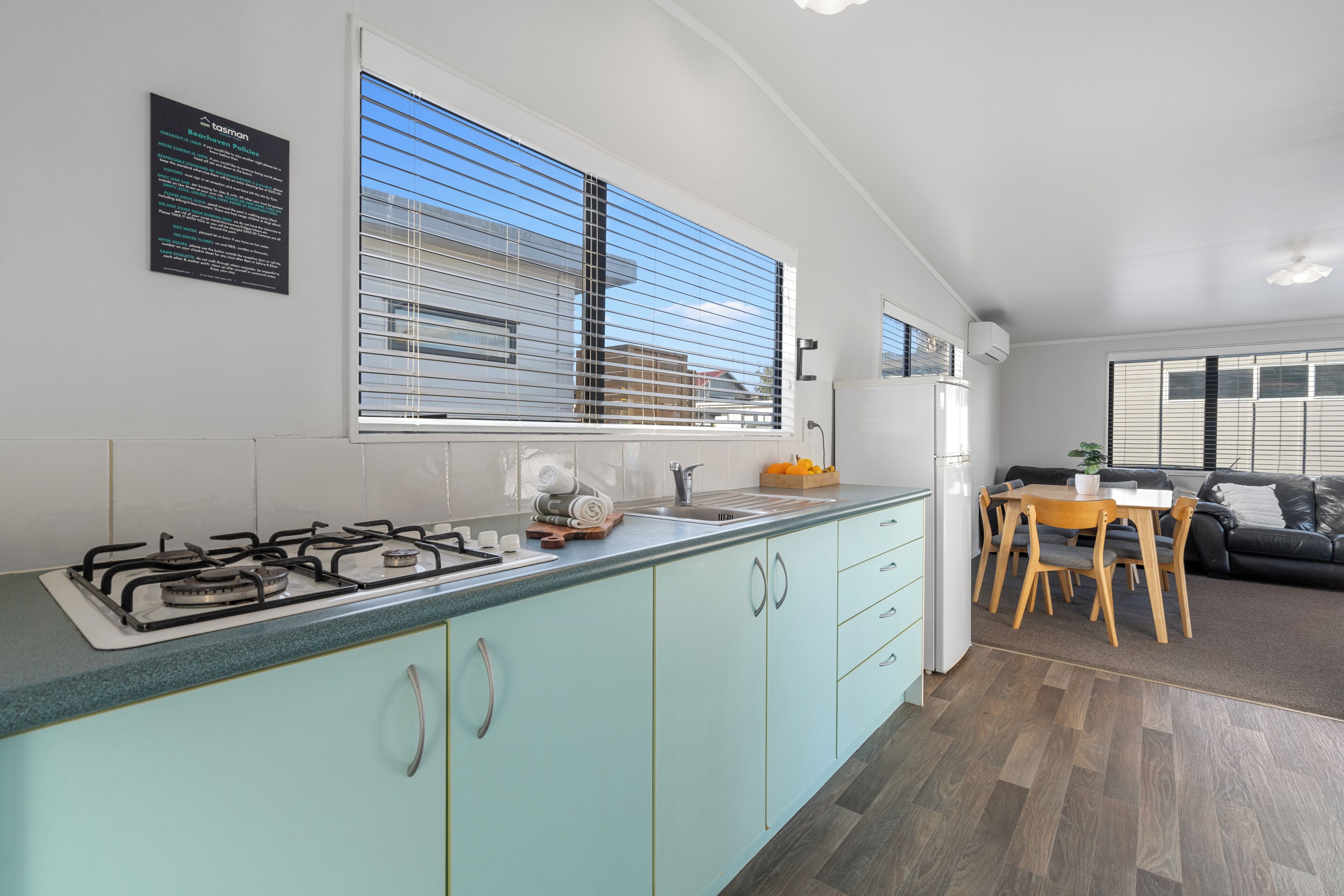 A modern kitchen with a gas stove, a sink, and a window with blinds. There is a dining area with a table and chairs.