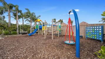 A playground with a blue slide, a red swing, and a wooden fence.