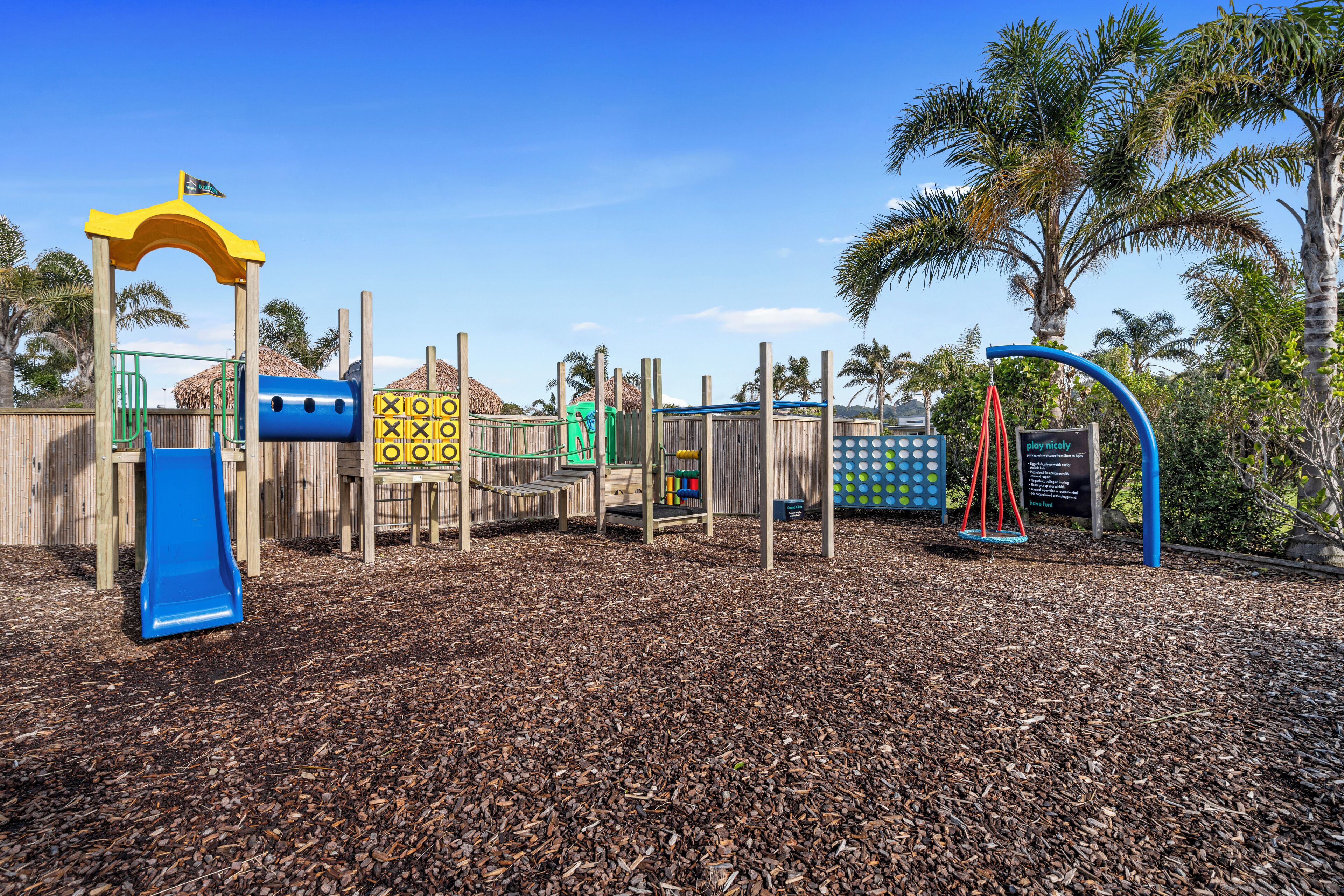 Un parque infantil con un tobogán azul, estructuras para escalar y columpios.