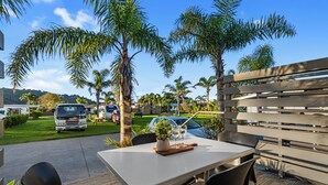 An outdoor seating area with a table and chairs, surrounded by palm trees and a wooden fence. - Tasman Holiday Parks – Beachaven (Waihi Beach)