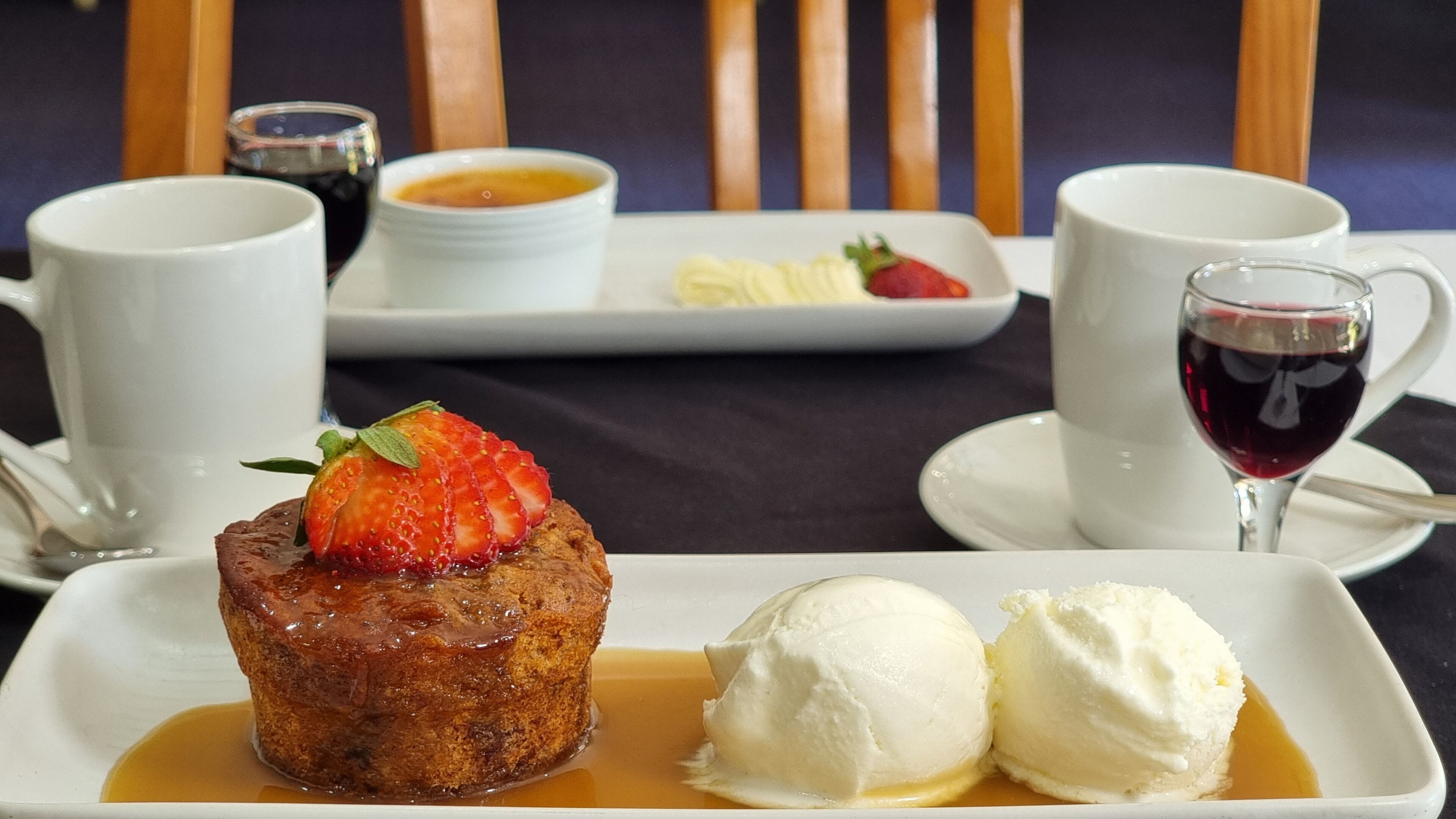 A dessert plate with a chocolate cake topped with a strawberry, two scoops of vanilla ice cream, and a small bowl of sauce.