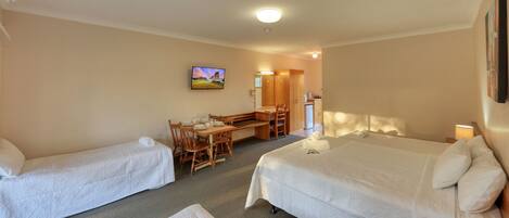 A hotel room with two single beds, a desk with a chair, a television, and a bathroom visible through an open door.