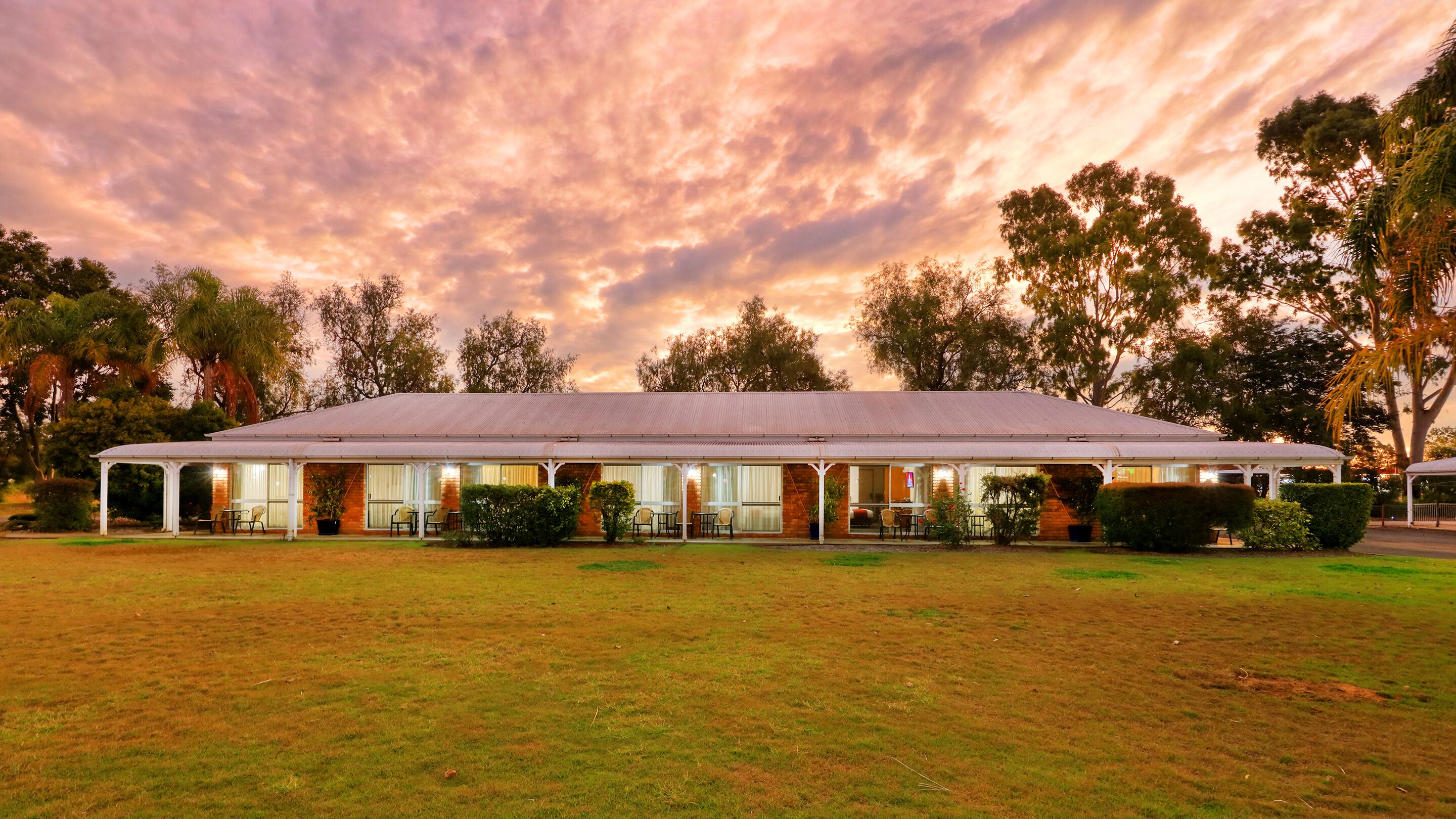 A large, single-story building with a flat roof, surrounded by a grassy lawn and trees.