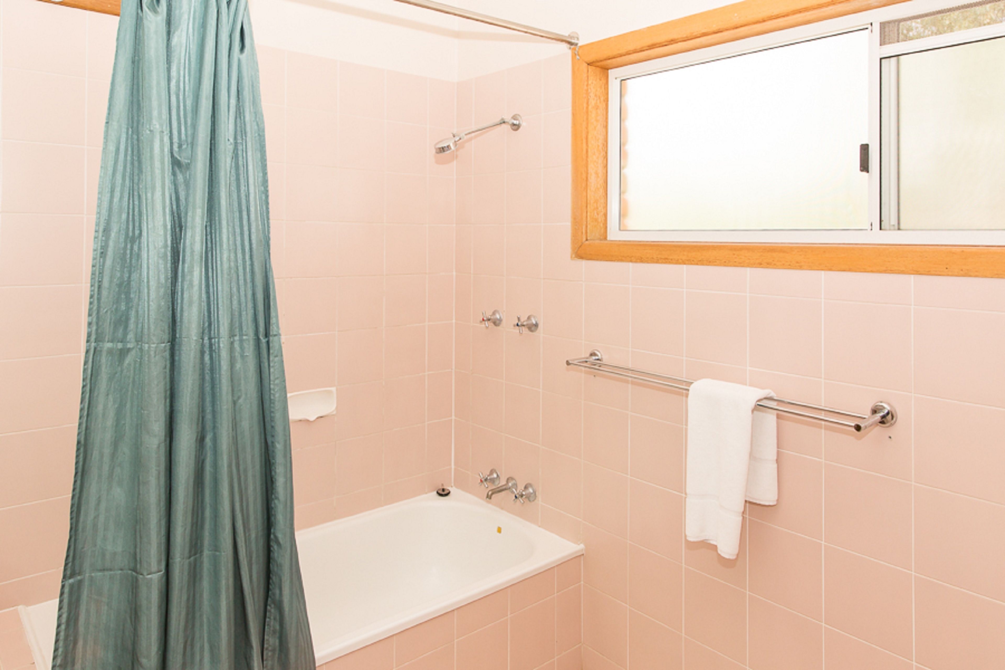 A bathroom with a bathtub, a shower curtain, a towel rack, and a window.