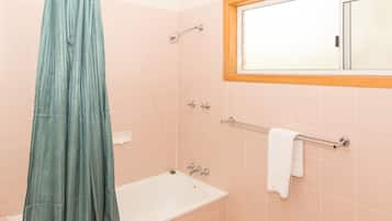 A bathroom with a bathtub, a shower curtain, a towel rack, and a window.