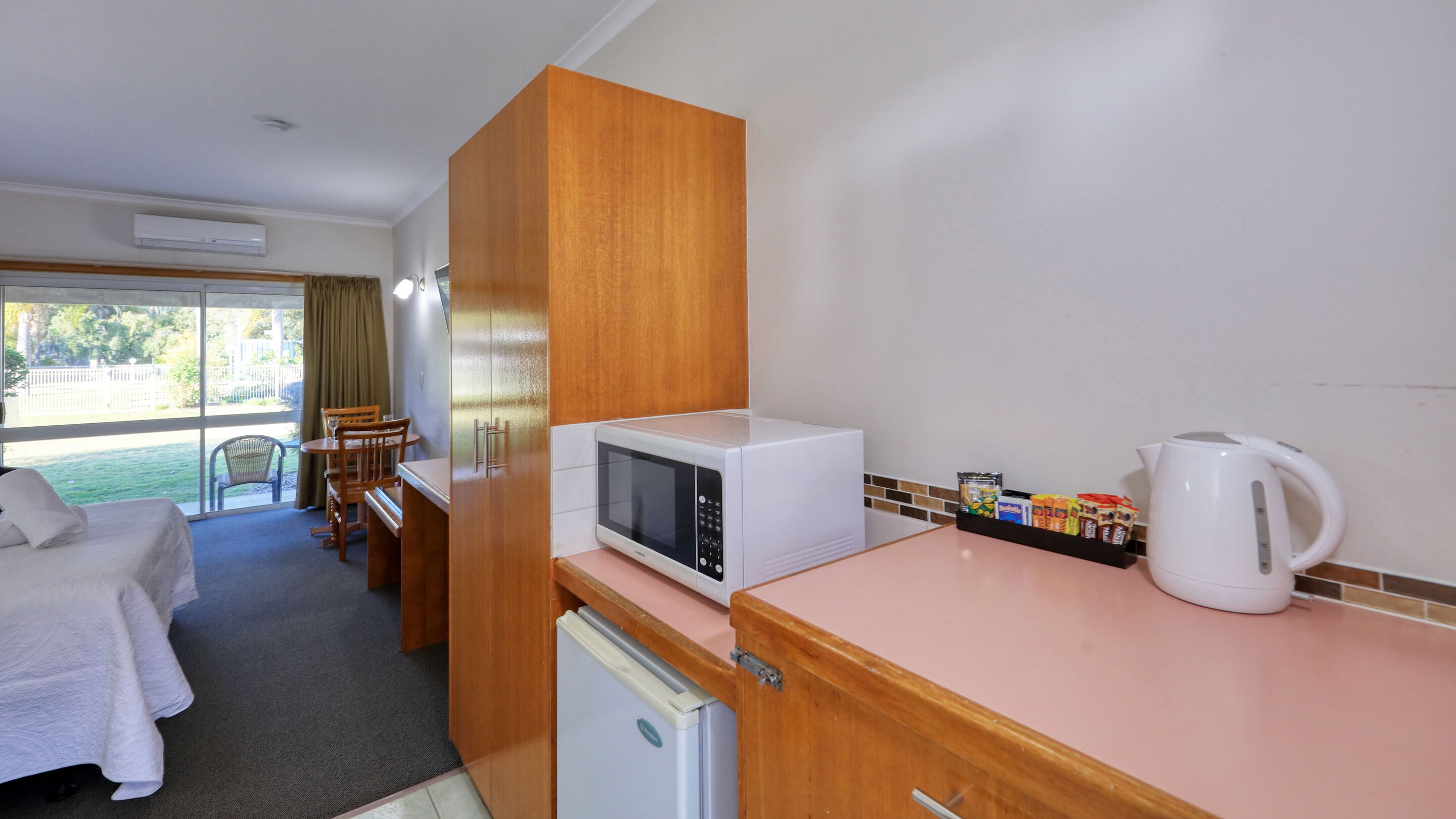Habitación de hotel compacta con kitchenette, cama, zona de comedor con mesa y sillas, y vistas al exterior a través de un amplio ventanal.