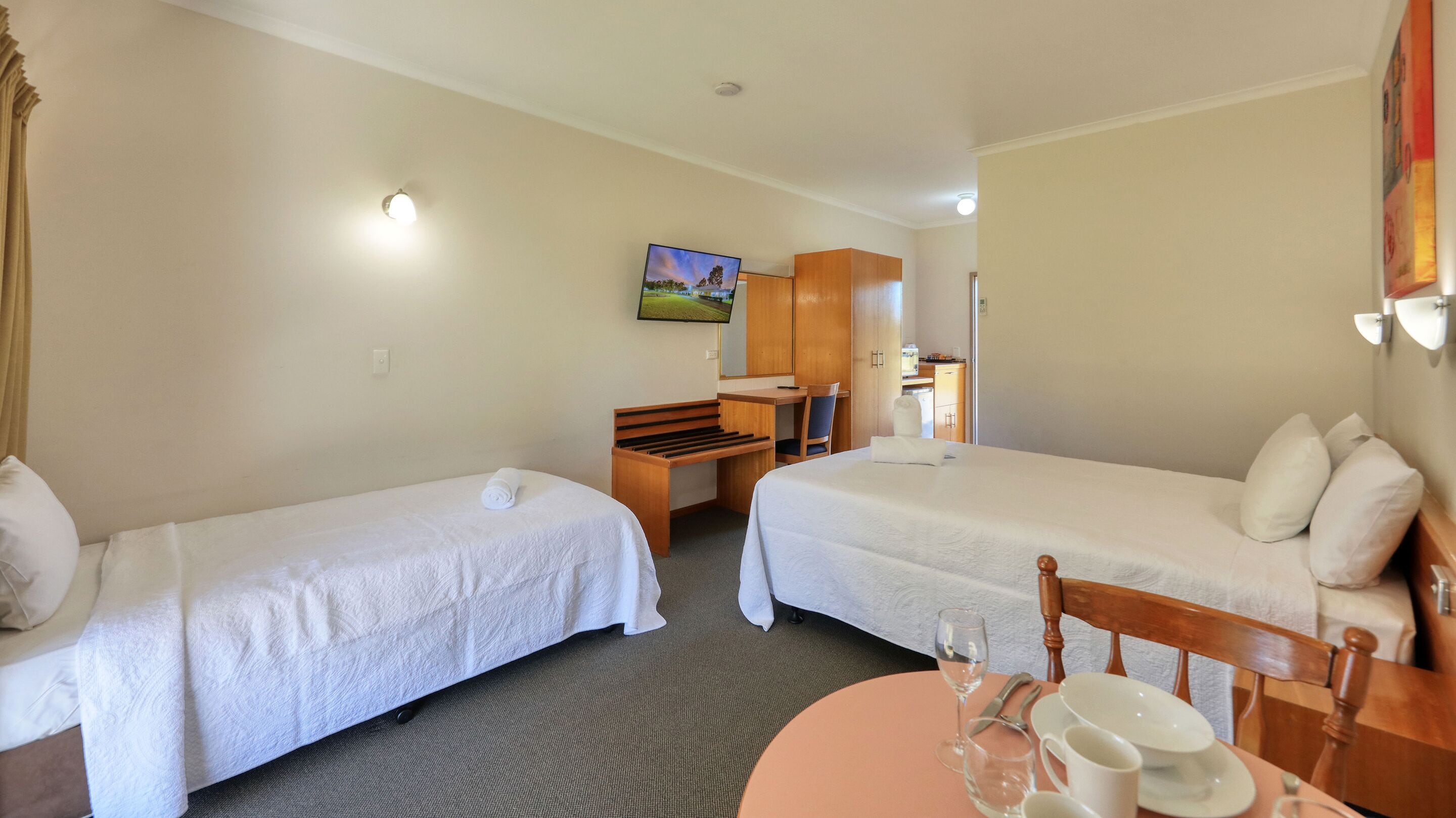 Ein Hotelzimmer mit zwei Einzelbetten, einem Schreibtisch mit Stuhl, einem Fernseher und einem kleinen Tisch mit einem Glas Wasser und einem Teller.