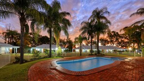 A swimming pool with a brick border, surrounded by a grassy area and palm trees. - Chinchilla Great Western Motor Inn (Chinchilla)