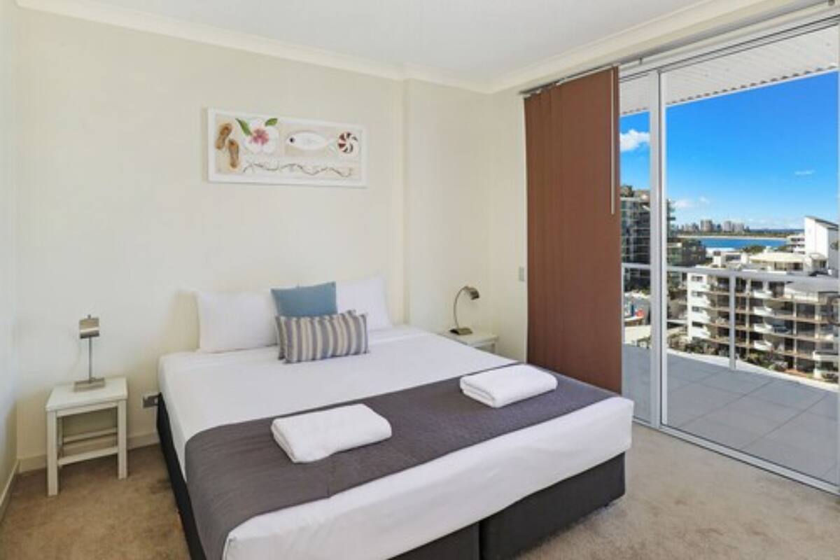 Una habitación de hotel moderna con una cama grande, una mesita de noche, una ventana con vistas a la ciudad y un balcón con puerta de vidrio.