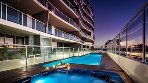 A modern hotel with a rooftop pool area, including a hot tub and a lounge area with a view of the city skyline. - Pandanus Mooloolaba (Mooloolaba)