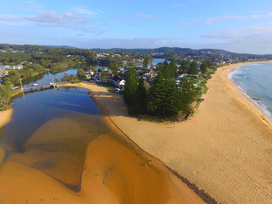 Vista aérea de una zona costera con playa, un puente y edificios residenciales.