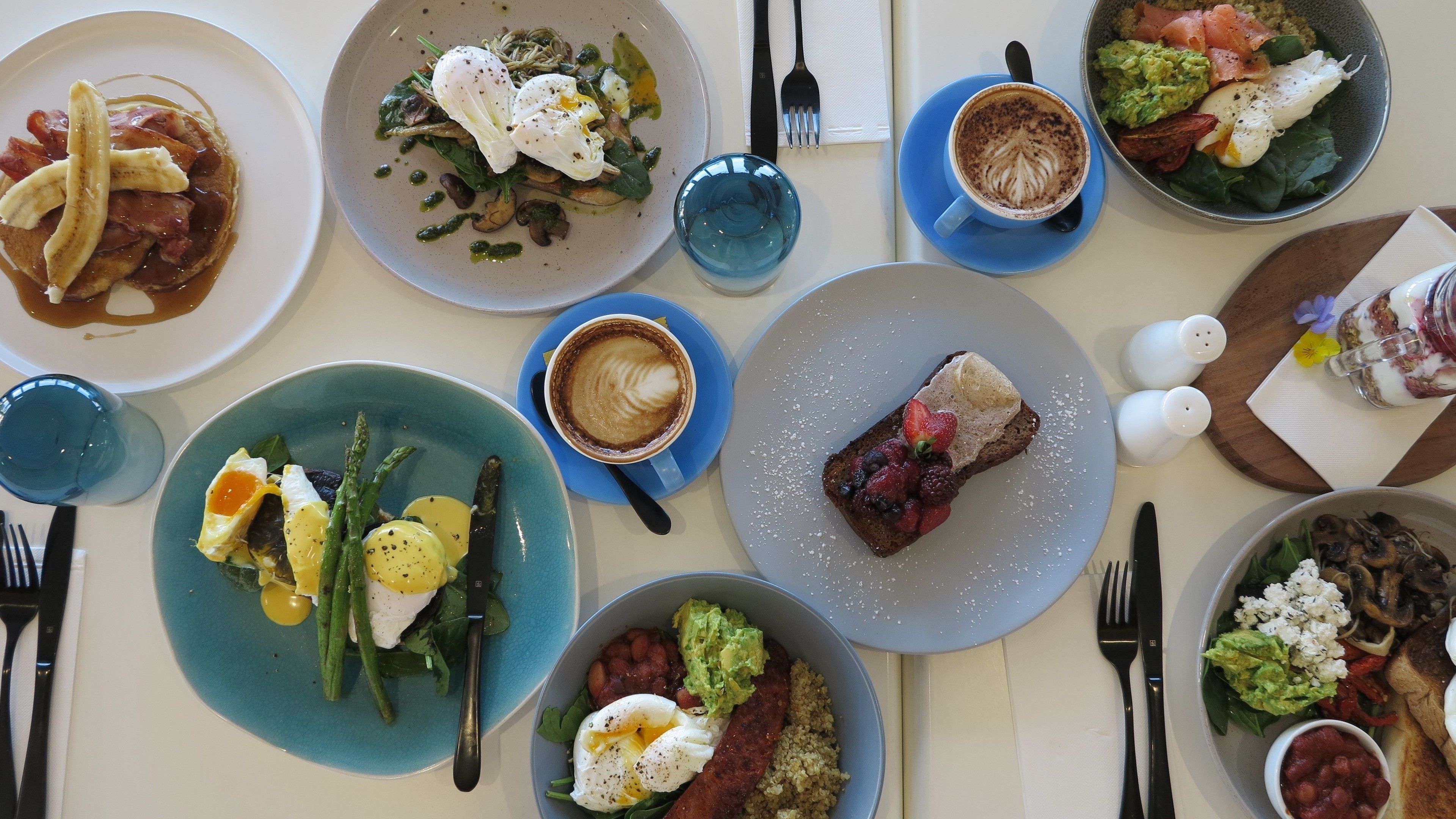 A table set with various dishes, including a plate with asparagus and eggs, a plate with a steak and berries, and a cup of coffee.