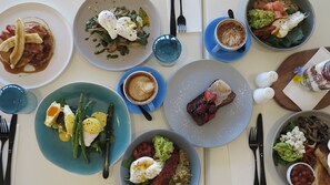 A table set with various dishes, including a plate with asparagus and eggs, a plate with a steak and berries, and a cup of coffee. - The Clan Terrigal (Wamberal)