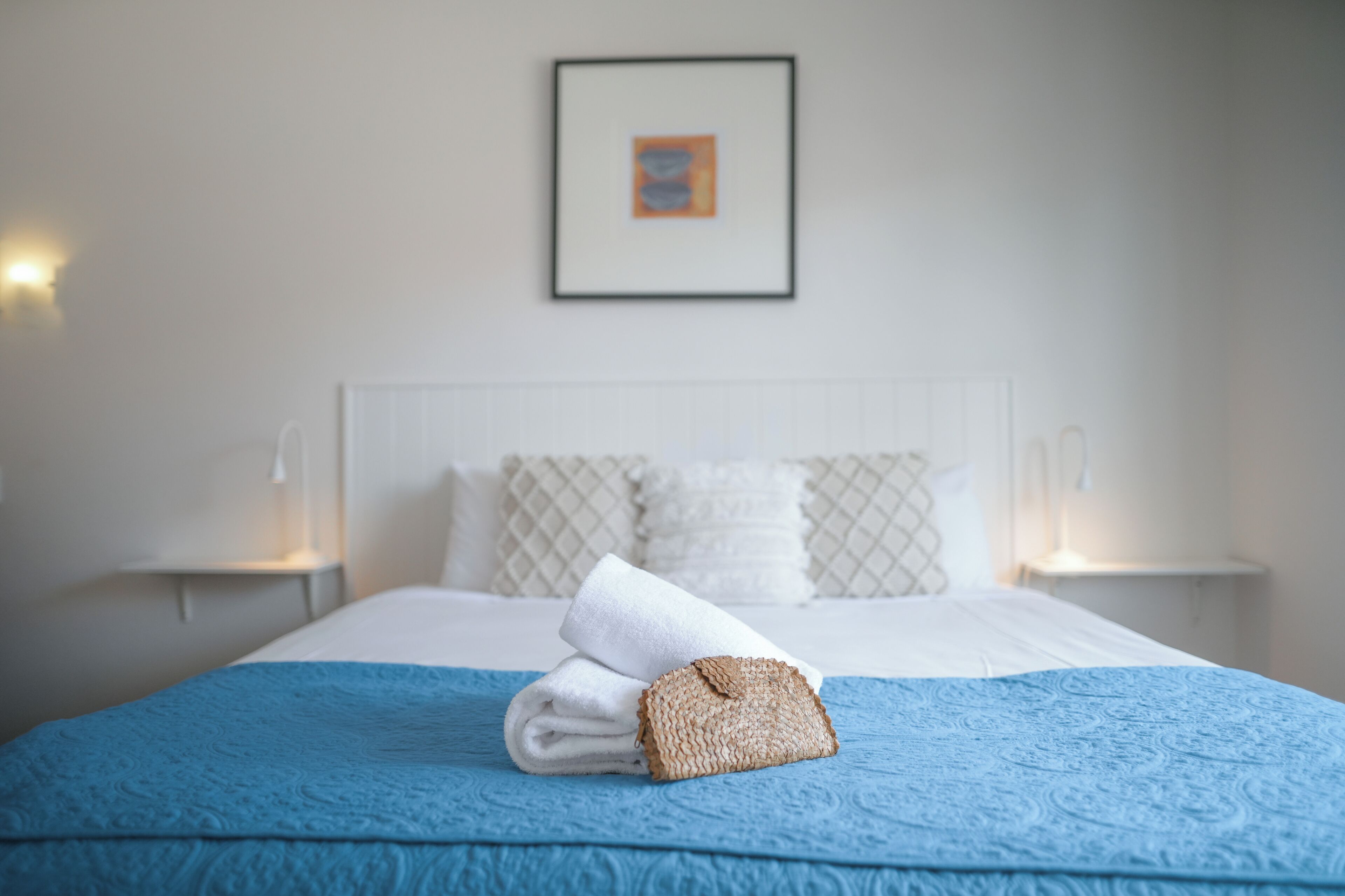 Una cama bien hecha con una colcha azul, almohadas blancas y una toalla doblada al lado.