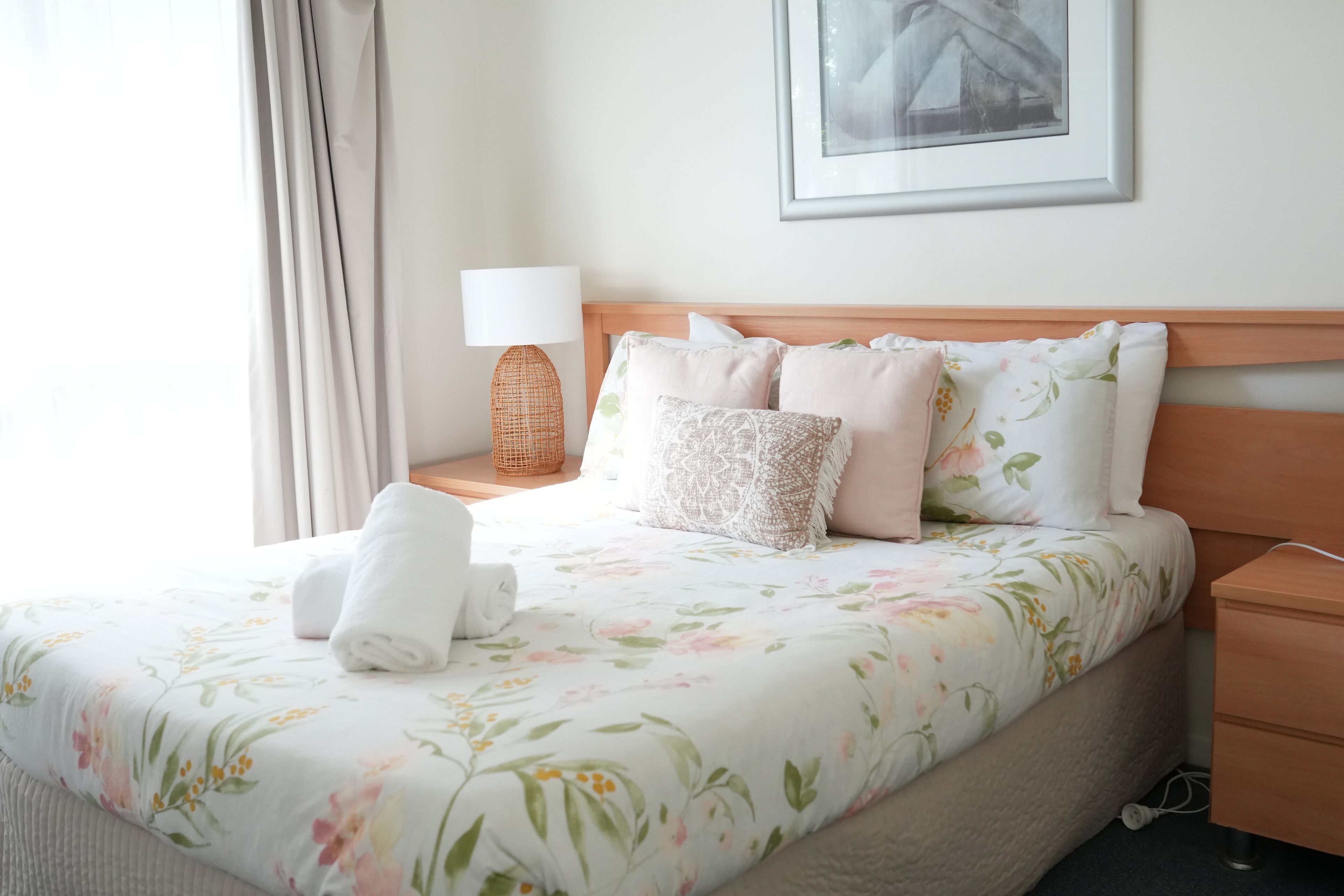 Uma cama bem arrumada com roupa de cama florida, uma luminária de mesa e um quadro na parede.