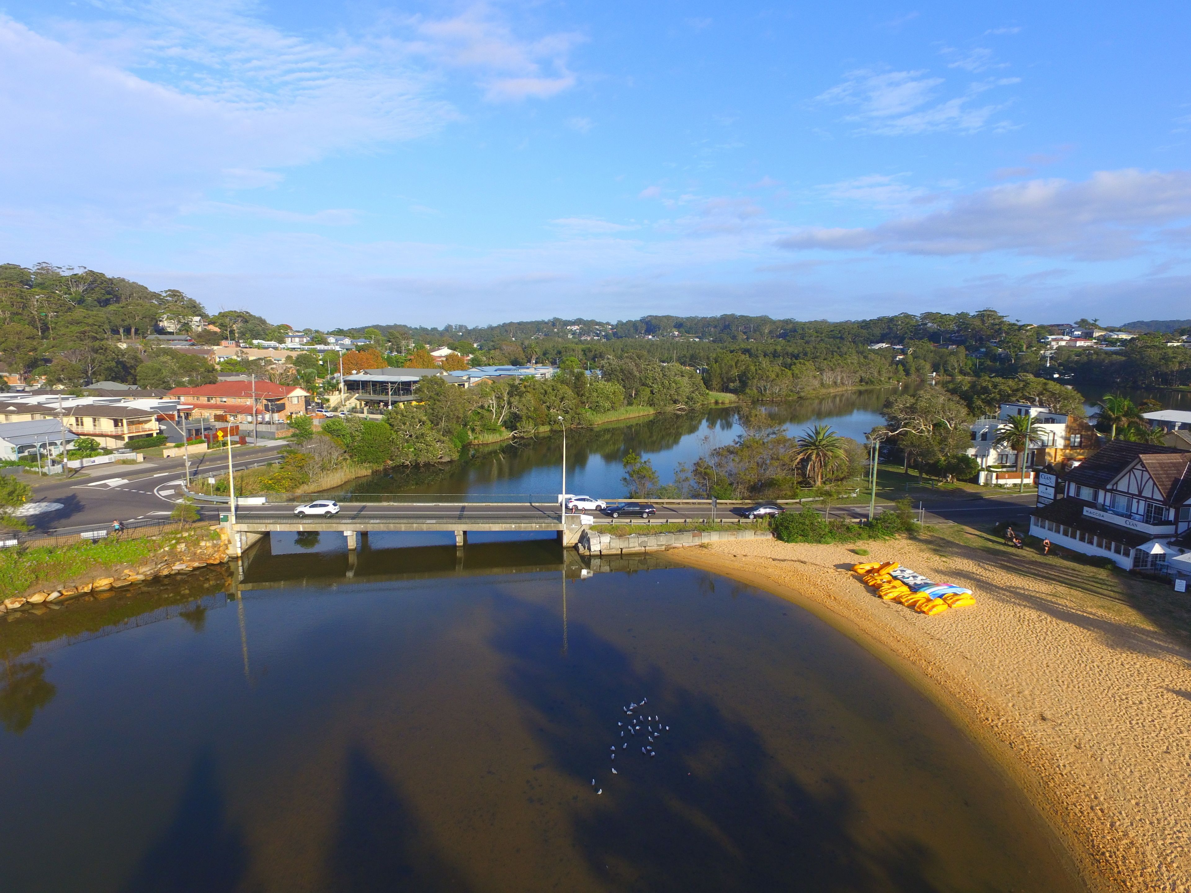 A riverside view with a bridge, buildings, and a sandy beach area.