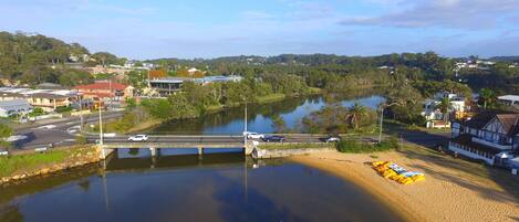 A riverside view with a bridge, buildings, and a sandy beach area.