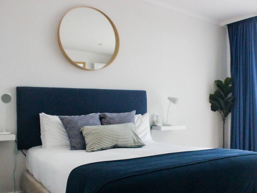 Una moderna camera d'hotel con un letto grande, uno specchio rotondo, un comodino e una pianta in vaso.