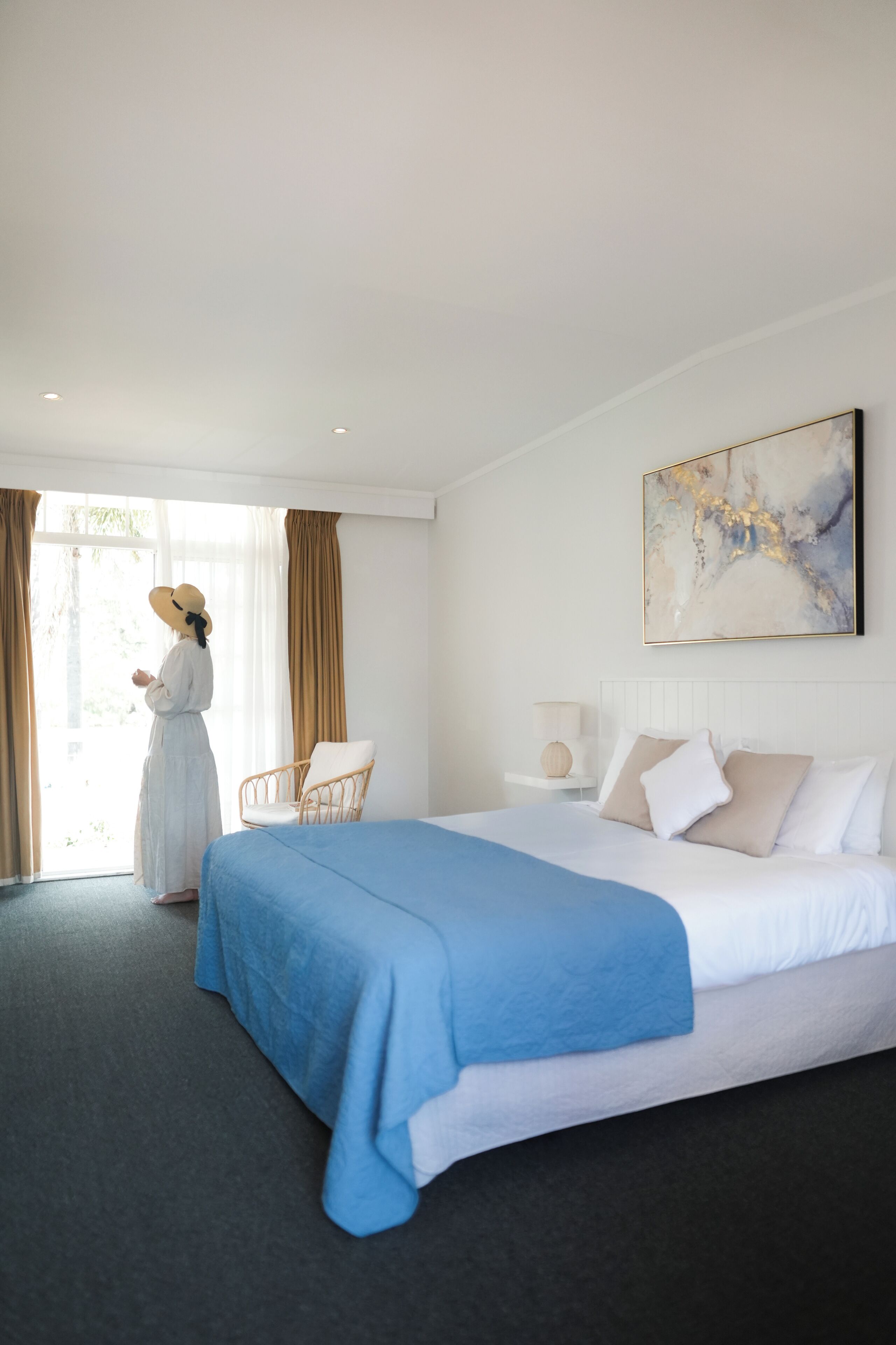 A hotel room with a large bed, a chair, a nightstand, and a window with curtains.