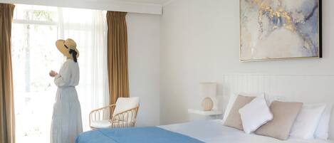 Een hotelkamer met een groot bed, een stoel, een nachtkastje en een raam met gordijnen.