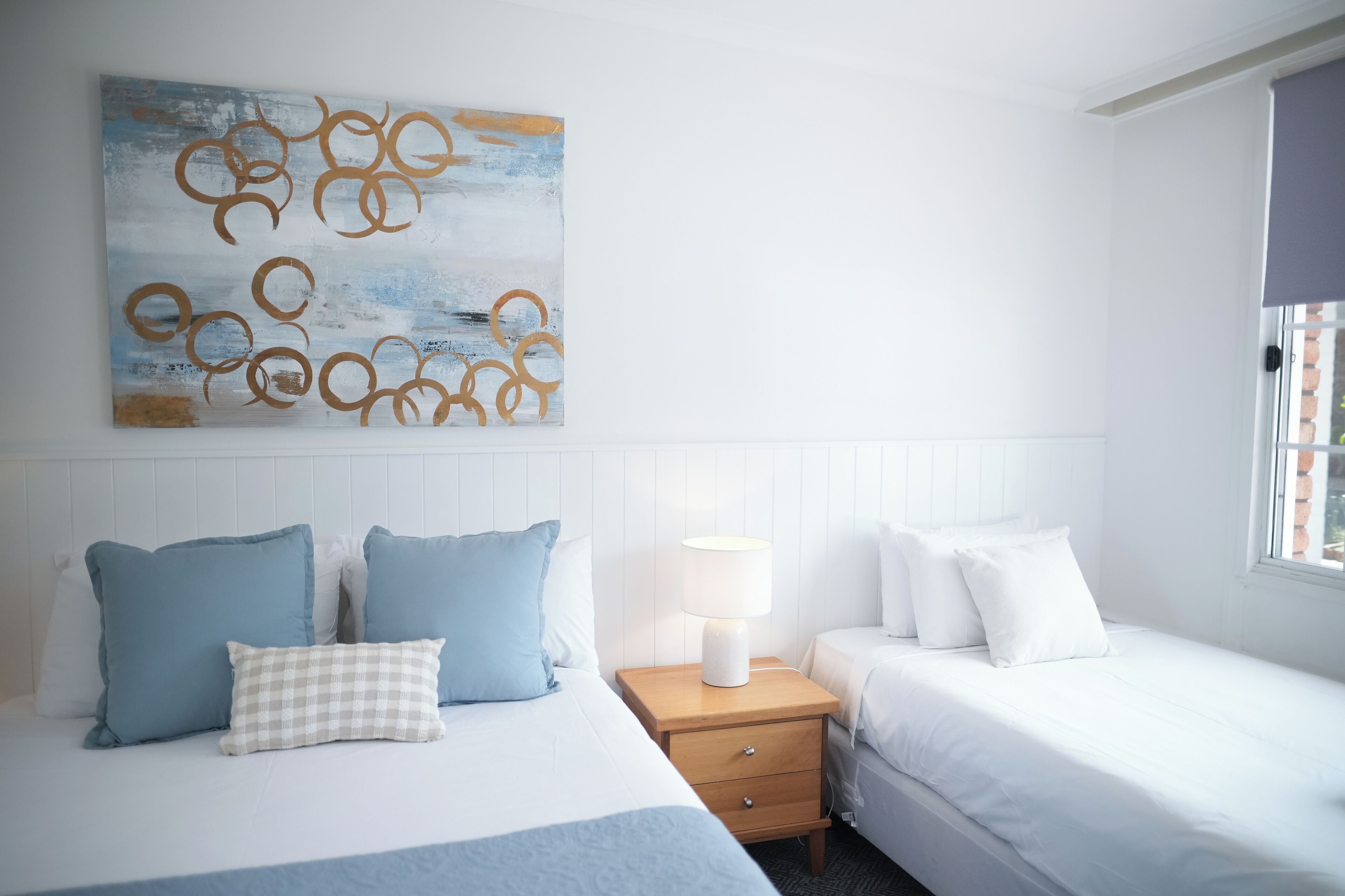 A hotel room with a bed, a nightstand, a lamp, and a wall art piece.