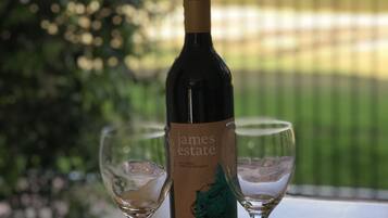 Una botella de James Estate Shiraz 2017 con dos copas de vino vacías sobre una mesa de madera, con un fondo exterior desenfocado.