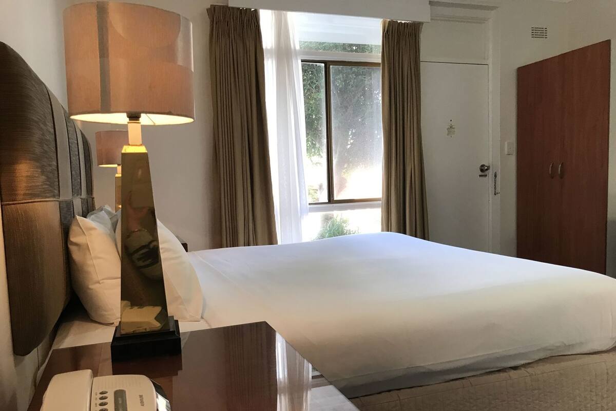 A hotel room with a bed, a bedside lamp, a phone, and a window with curtains.