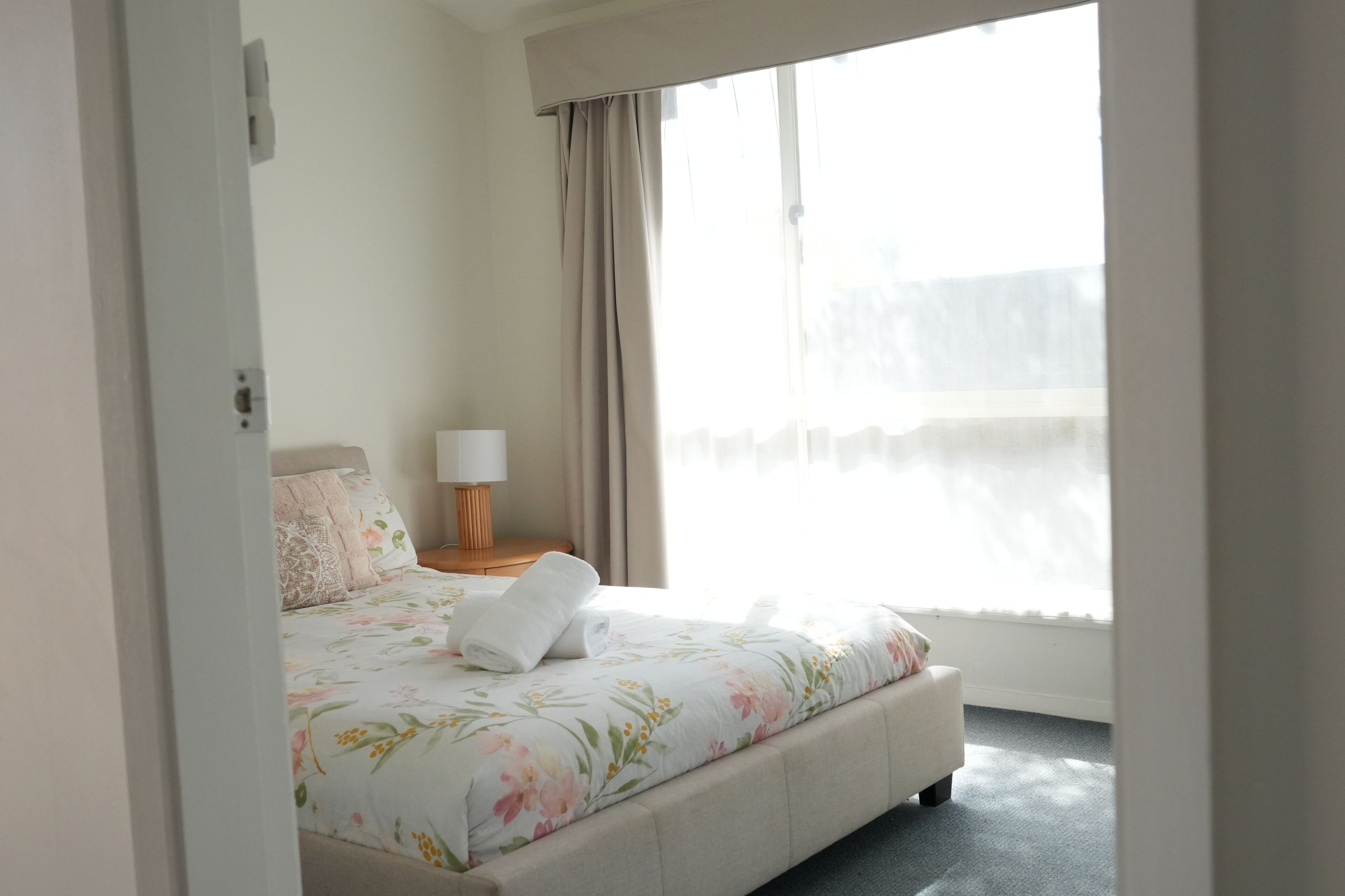 Habitación de hotel con cama, mesita de noche, lámpara y ventana con cortinas.