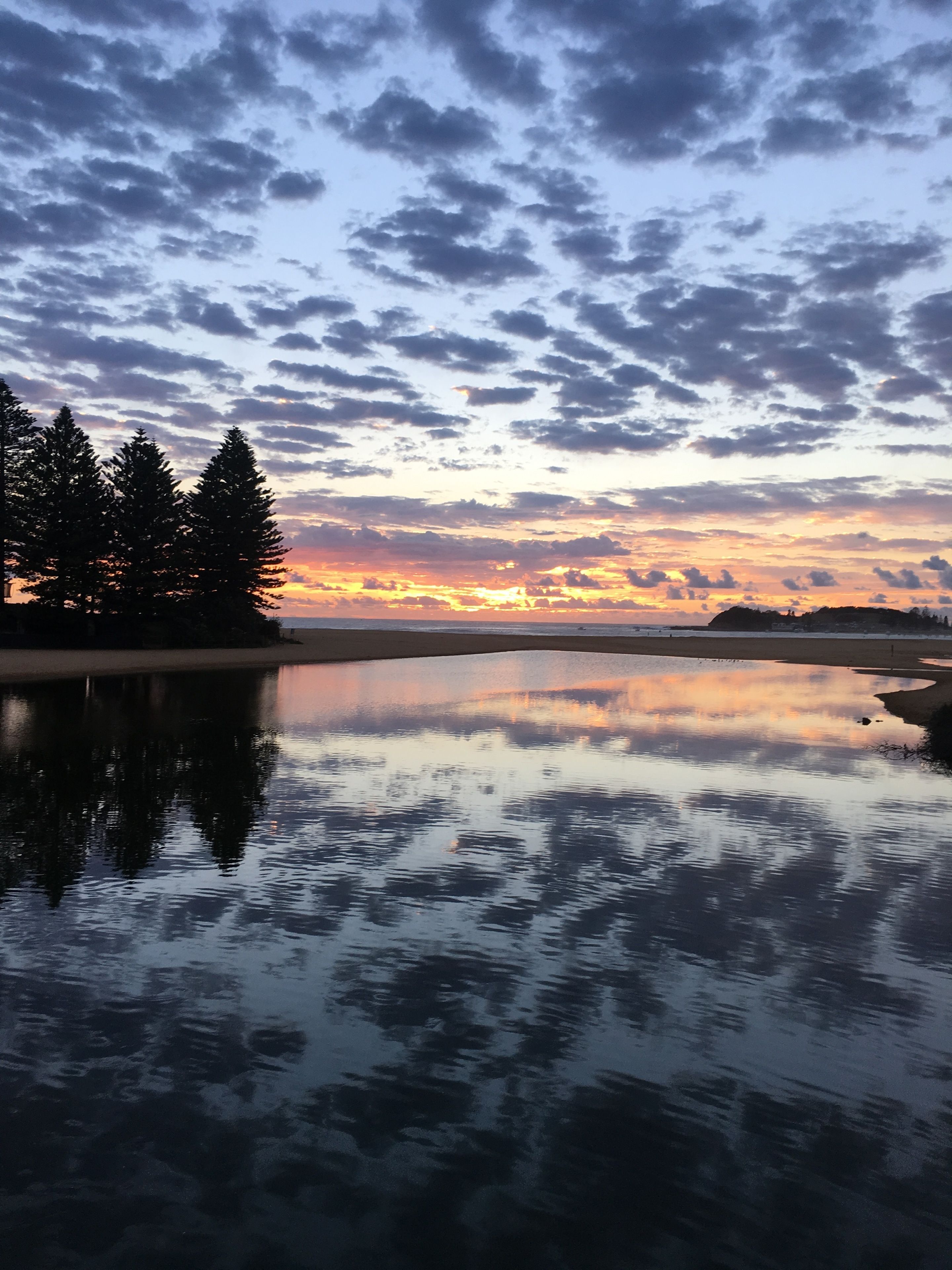 A calm lake reflecting the sky with clouds, surrounded by trees.
