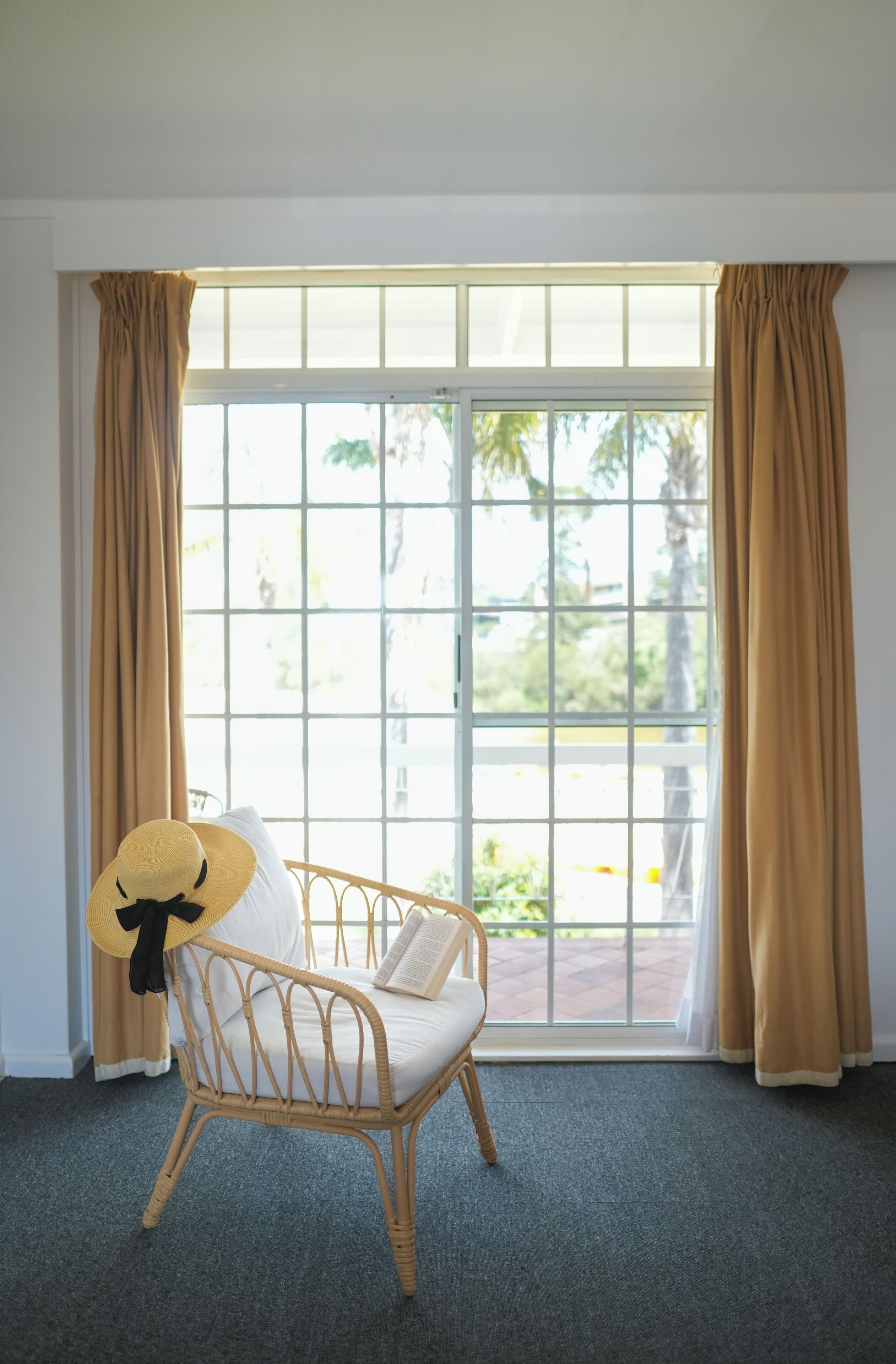 A wicker chair with a cushion and a book, positioned near a window with beige curtains.