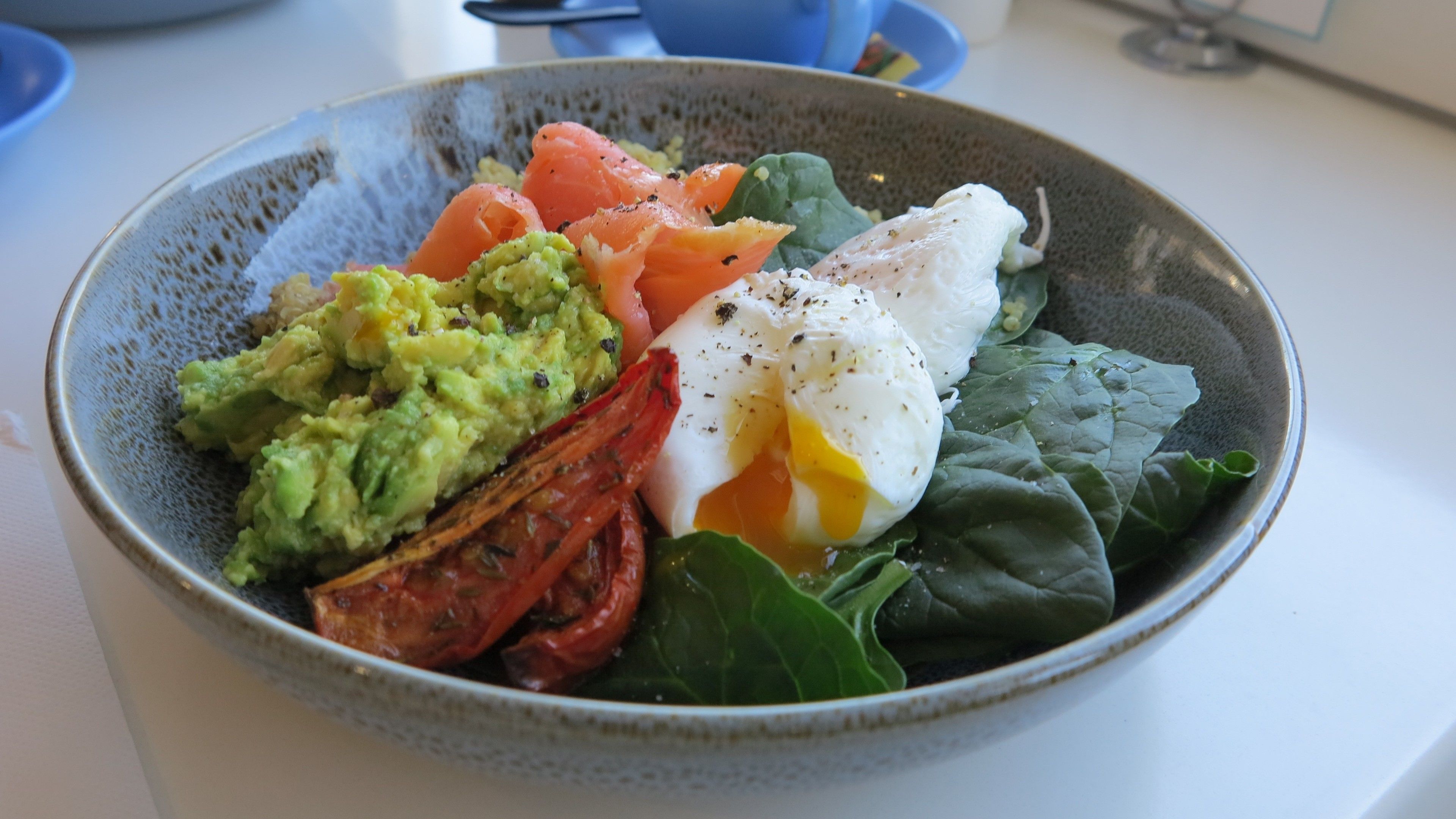 A bowl of food with avocado, smoked salmon, a poached egg, and greens.