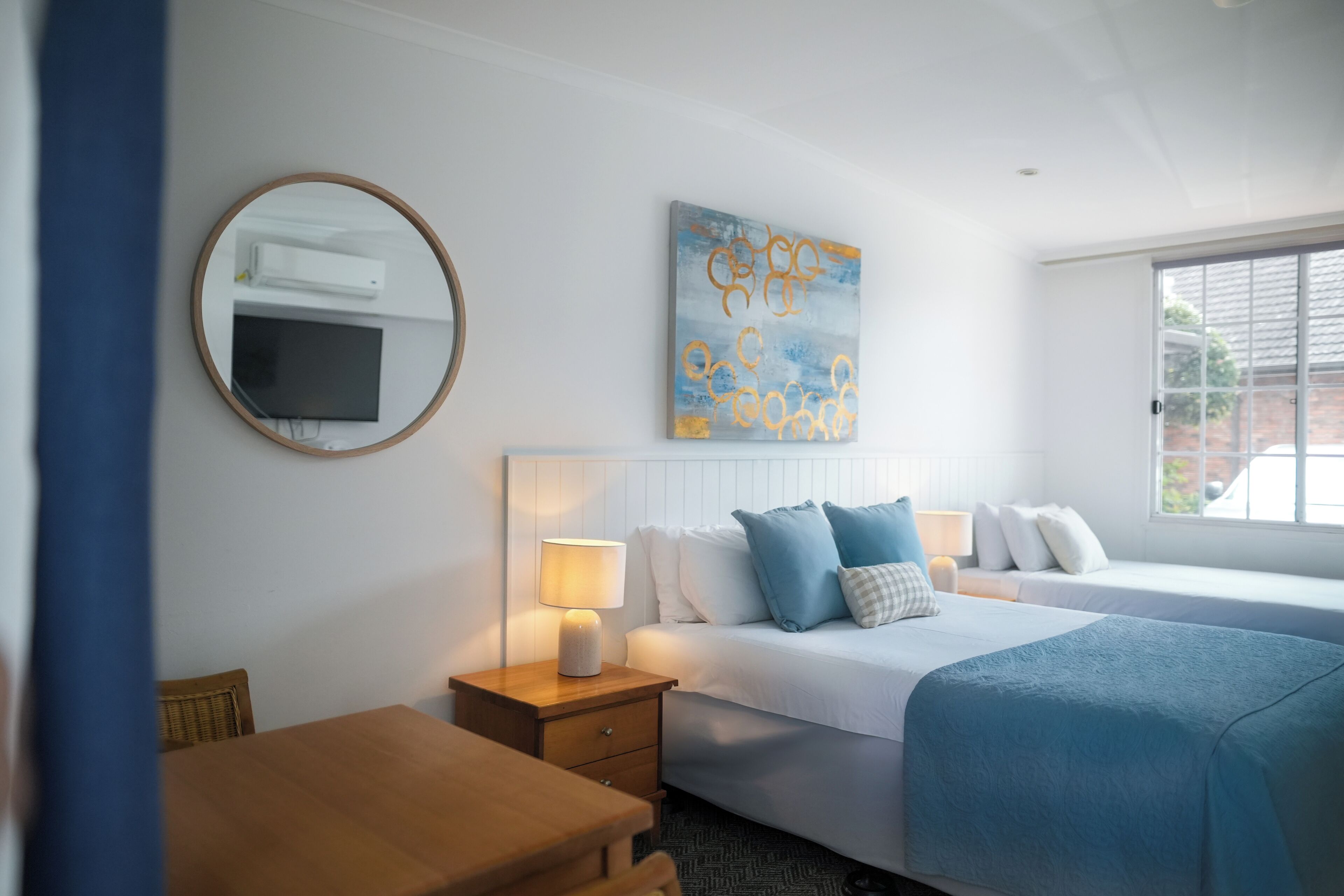 A hotel room with a bed, bedside tables, a mirror, a flat-screen TV, and a window.