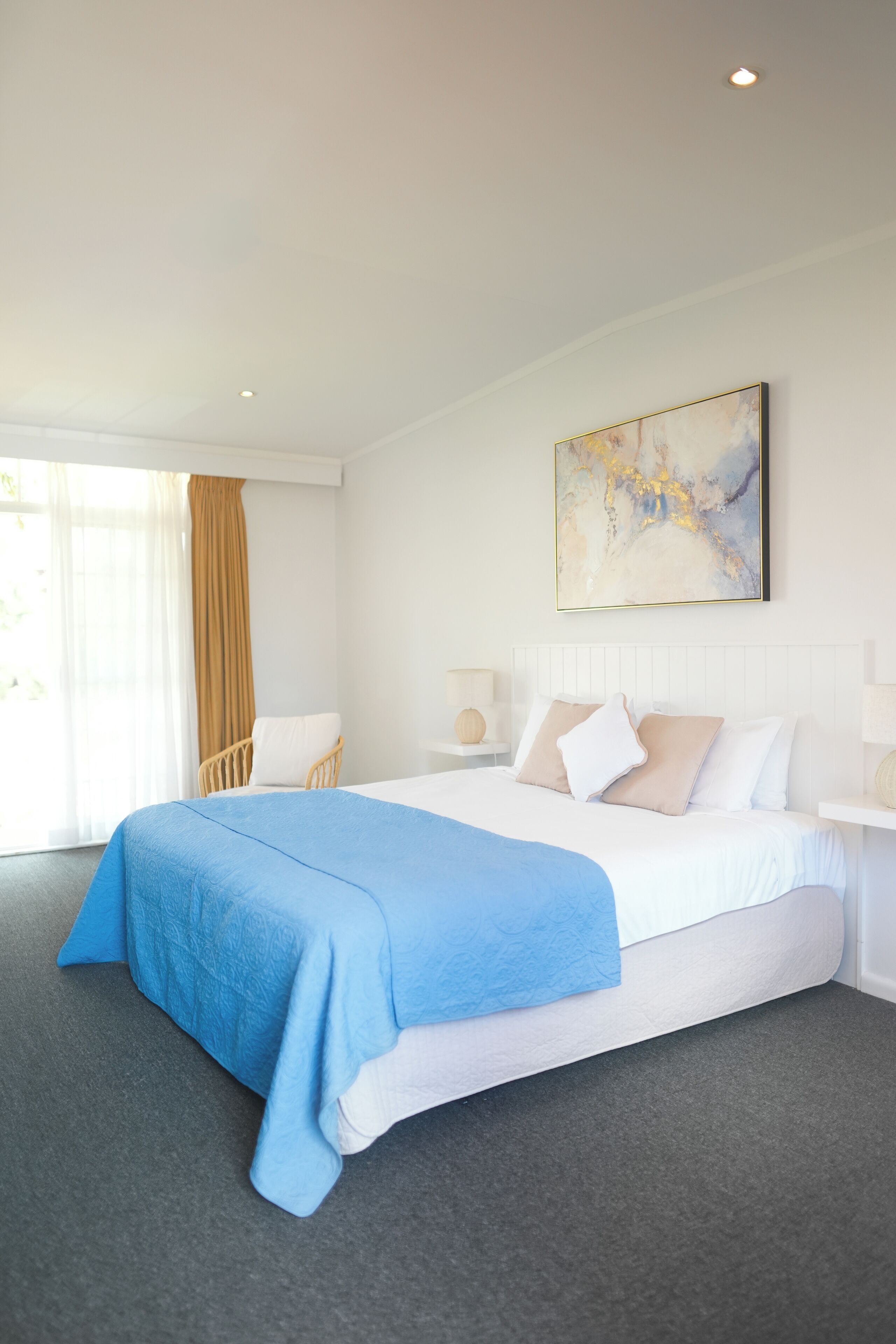 Quarto de hotel com uma cama grande, uma cadeira, uma mesa de cabeceira e um quadro na parede.