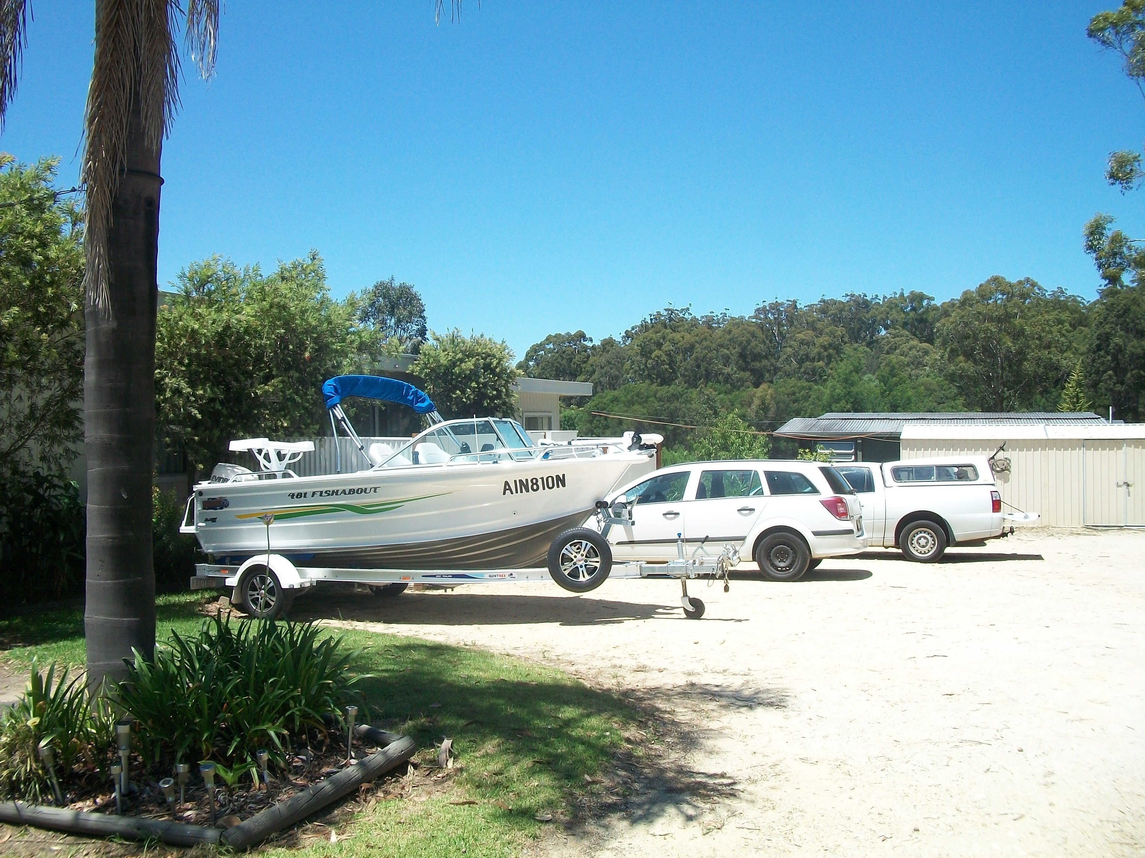A boat named 'Ain810N' parked in a sandy area with a white car and a building in the background.