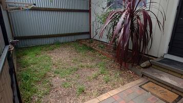 A backyard with a paved patio, a metal fence, and a house with a window.